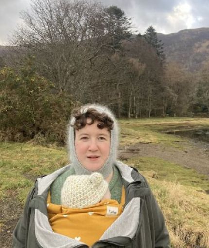  Portrait of a person outdoors by a lakeside woodland landscape, carrying a baby in a front carrier