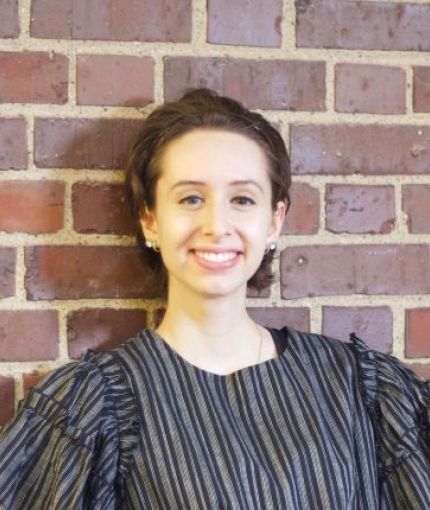 Person smiling and posing against brick wall.