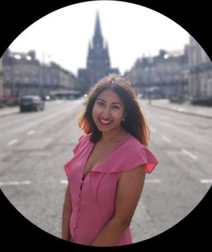 An image of Sahara Choudhury smiling, in a pink dress with a blurred Edinburgh background. 