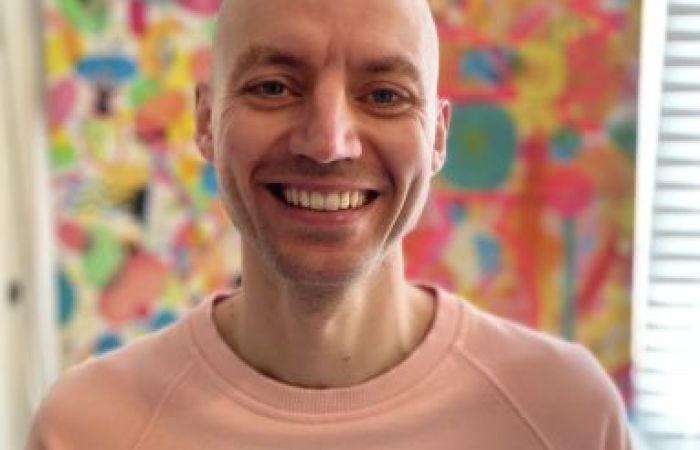 Image of Dan Castro smiling in front of a brightly coloured abstract artistic background