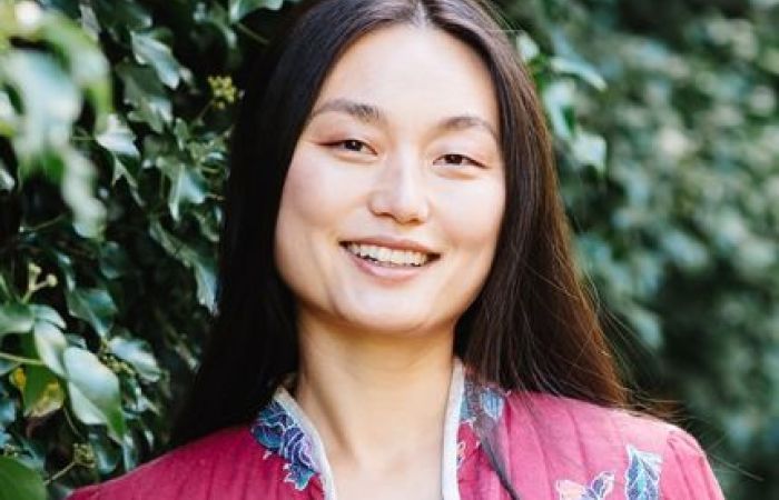 A Chinese-American woman in a red jacket standing in front of a wall of ivy