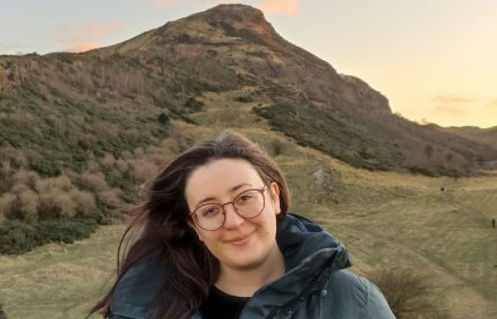 A photo of a woman smiling, standing in front of a hill