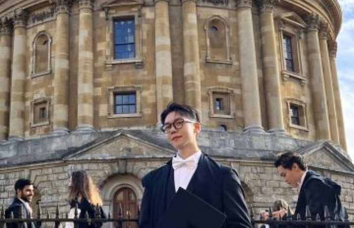 Outdoor portrait of Taehwan Kim in academic attire, standing in front of a historic library building.