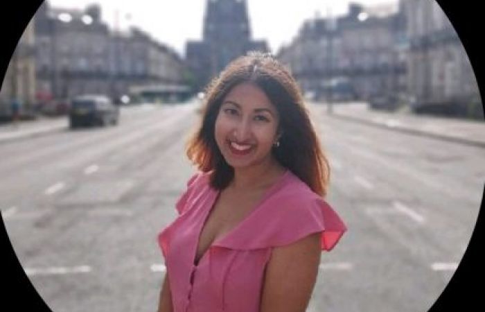 An image of Sahara Choudhury smiling, in a pink dress with a blurred Edinburgh background. 